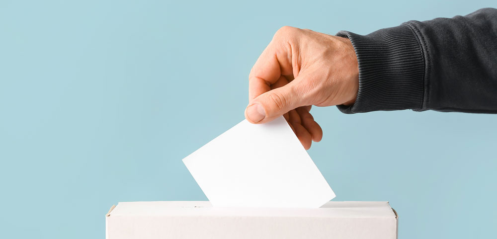 Main d'une personne qui place un bulletin de vote dans une urne